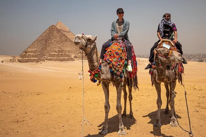 Two riders on decorated camels below the Giza pyramids on an 8-day luxury Egypt tour, Giza, Egypt